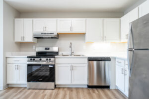 Bright modern kitchen with white cabinets and stainless steel fridge, dishwasher, range, and sink.